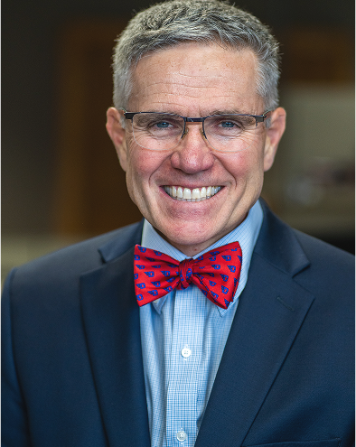 Smiling man in glasses and suit with red bow tie.