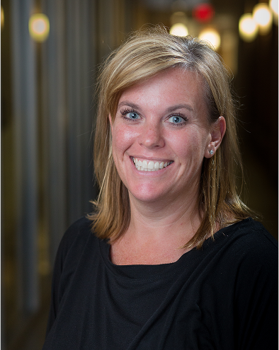 Smiling woman with shoulder-length blond hair in a hallway.