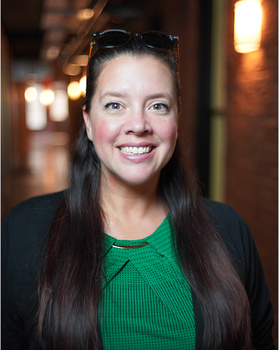 Smiling woman in a green shirt with long hair indoors.