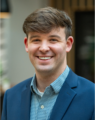 Smiling man in a blue blazer and checkered shirt.