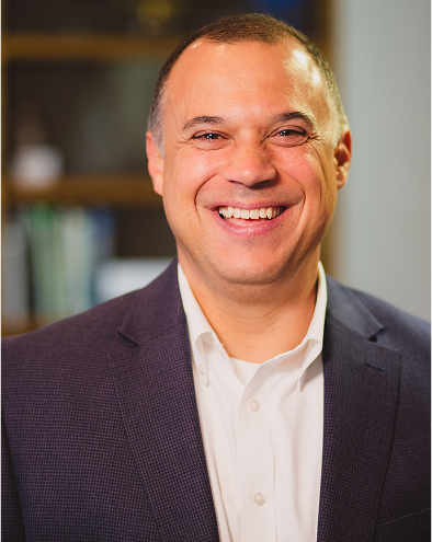 Smiling man in a suit and white shirt, indoor setting.