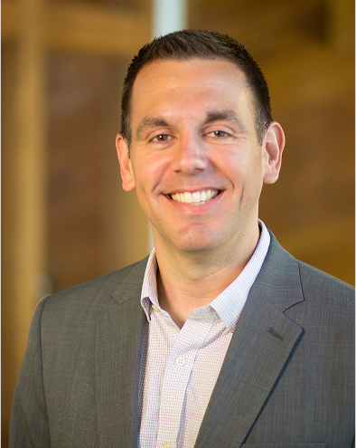 Smiling person in a suit with a blurred brown background.
