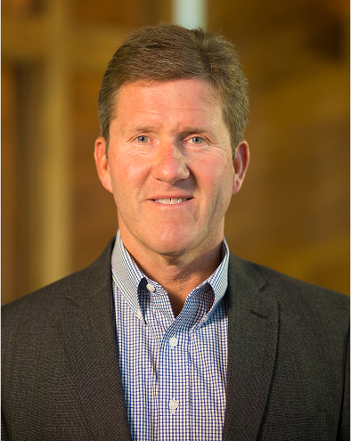 Man in a suit smiling, blurred background.