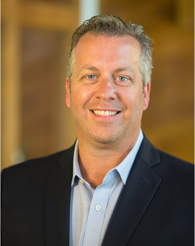 Smiling man in a suit jacket against a blurred background.