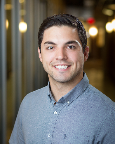Smiling person in a hallway, wearing a grey shirt.