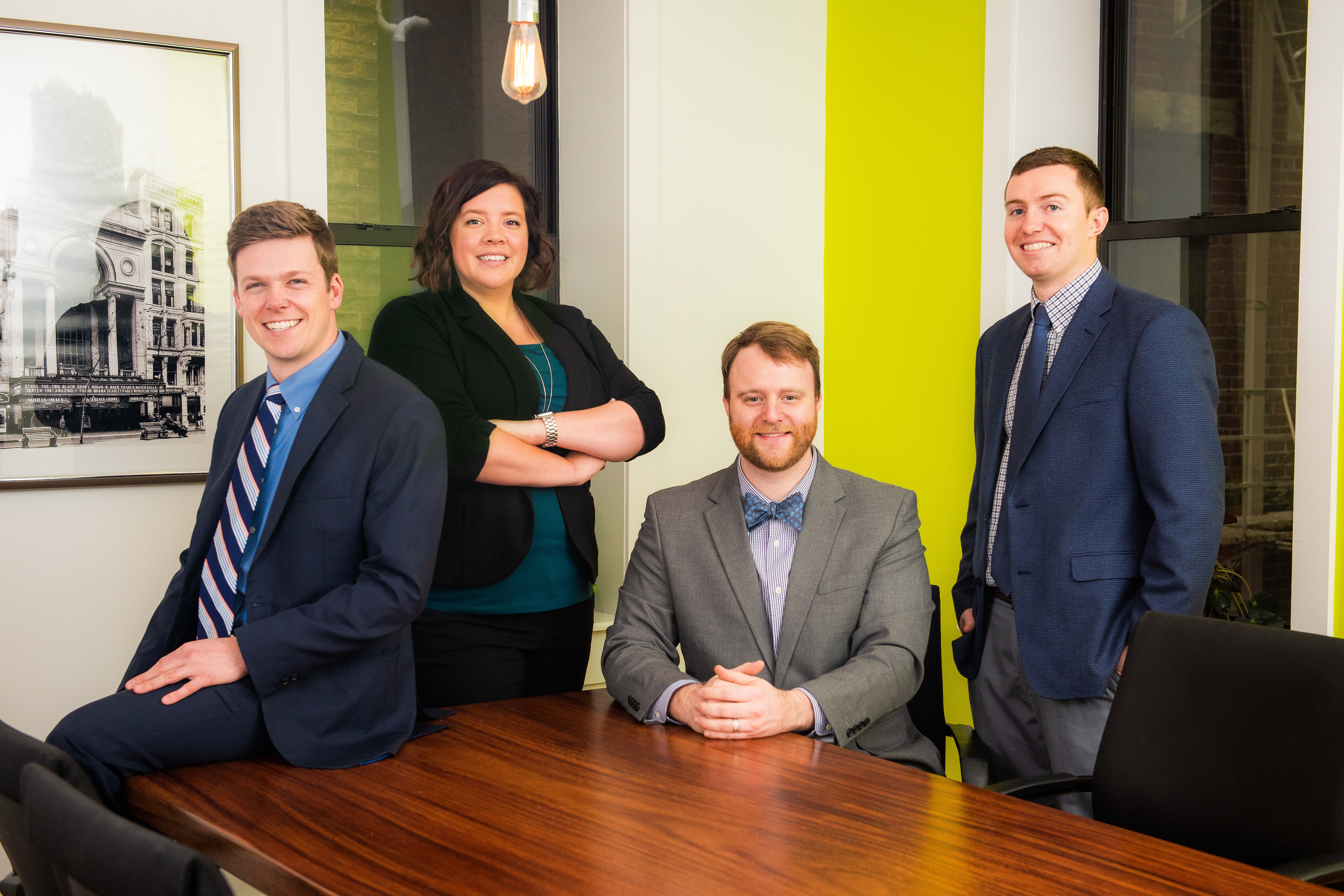 Four people in business attire smiling in a modern office setting.
