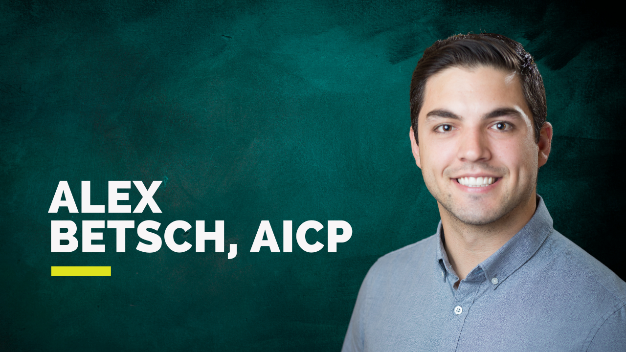 Smiling man in a button-up shirt with a dark teal background.