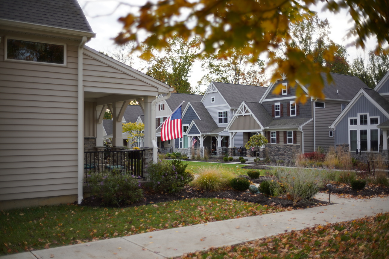 Suburban street with houses, American flag, and autumn leaves.