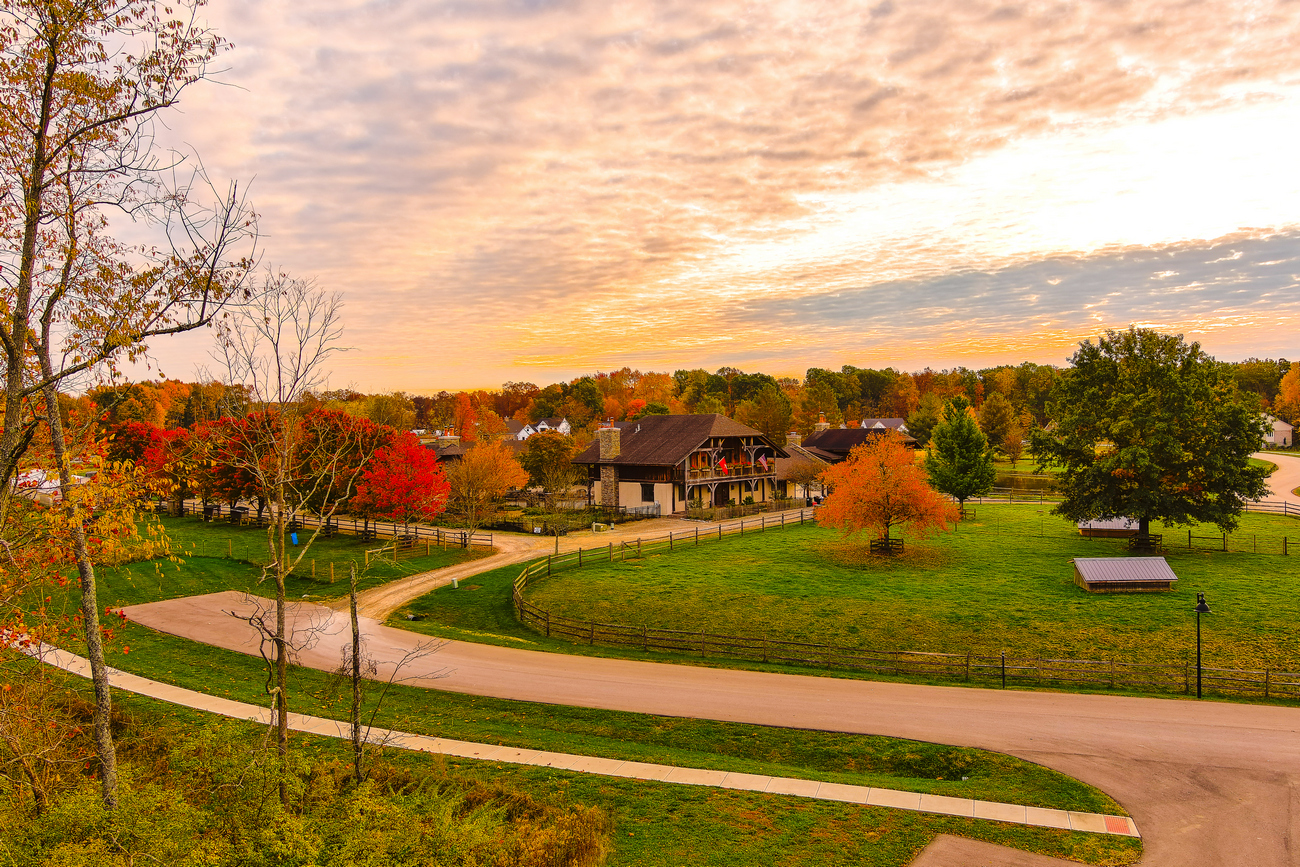 Autumn landscape with colorful trees, winding path, and a cozy house under a golden sky.