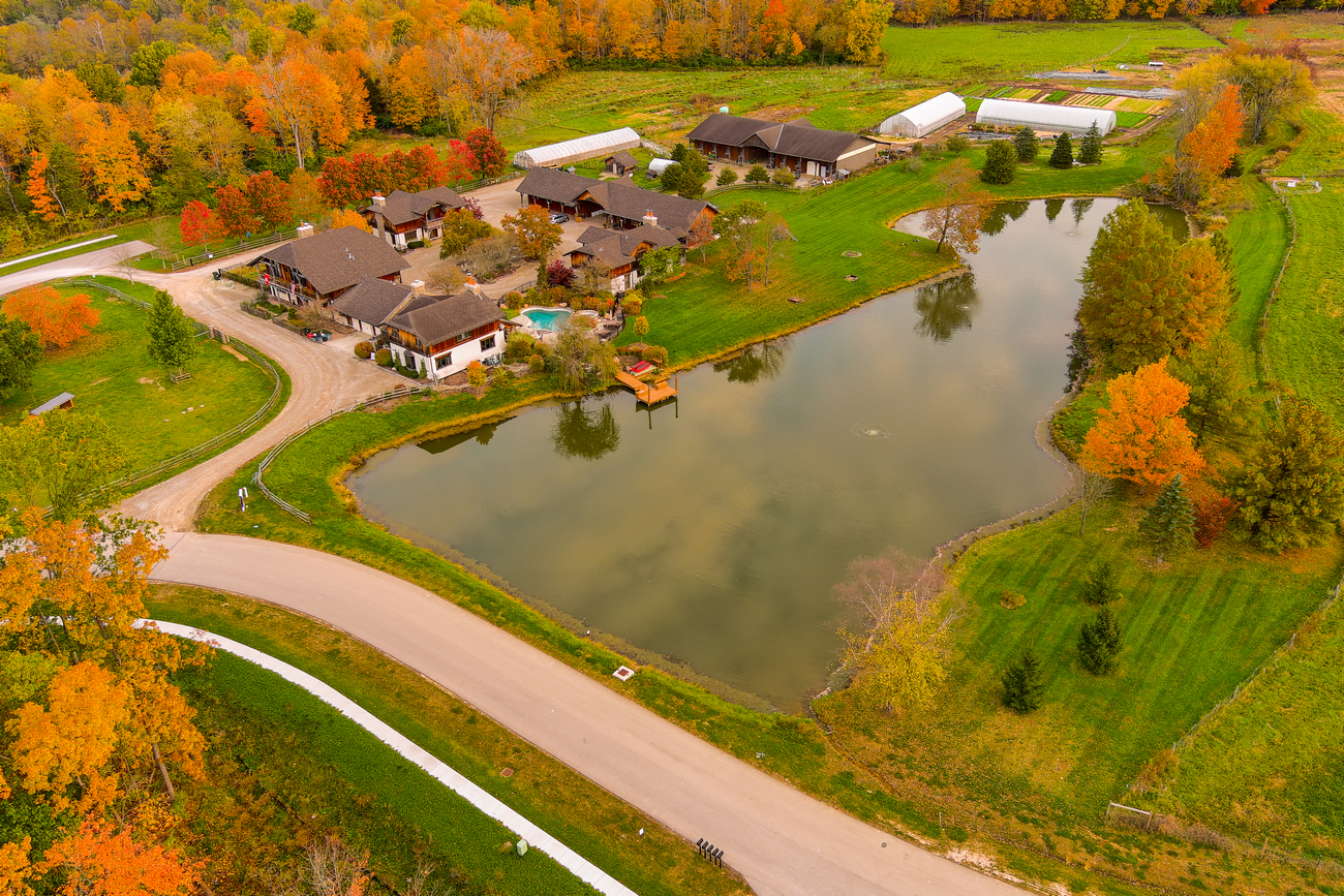 Aerial view of houses by a pond surrounded by colorful autumn trees.