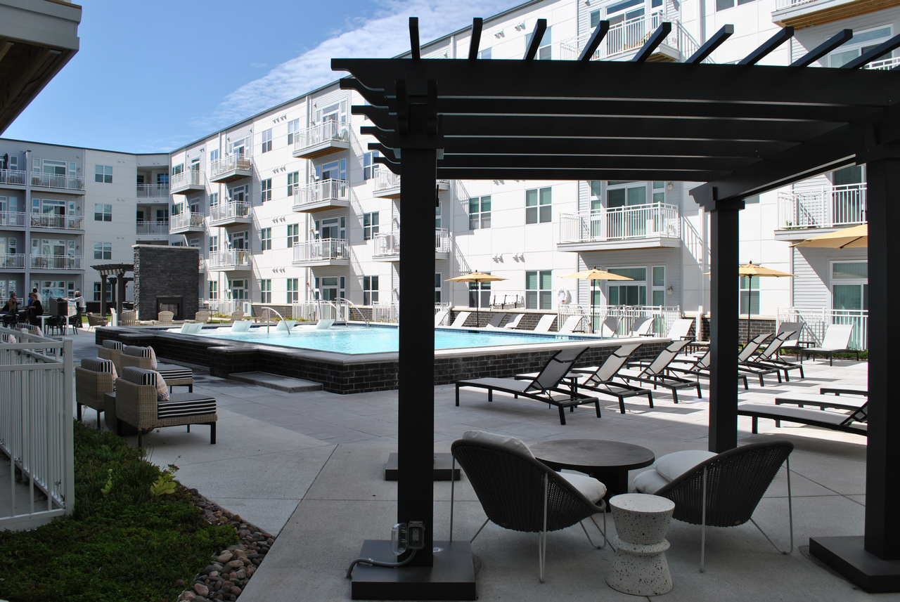Apartment courtyard with pool, lounge chairs, and umbrellas under a clear sky.