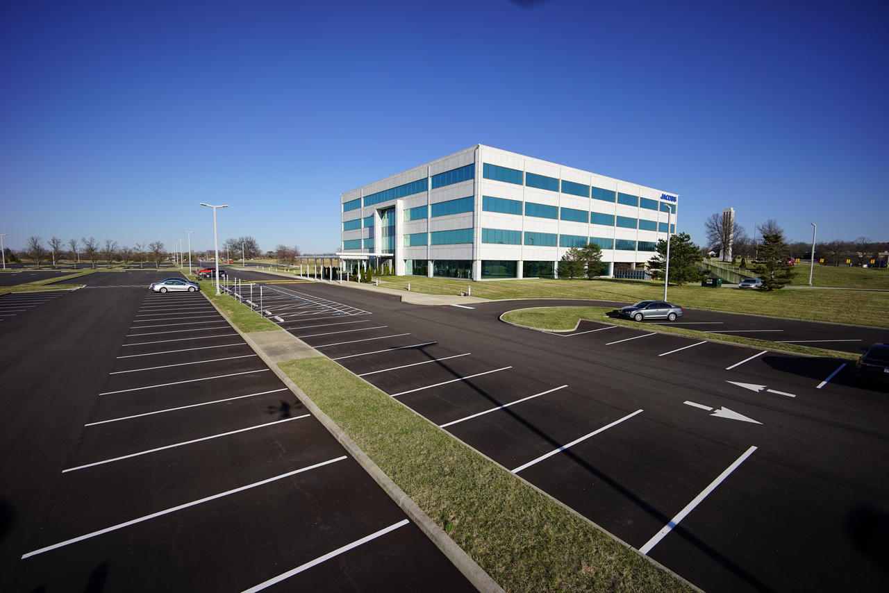 Empty parking lot with a large, modern office building under a clear blue sky.