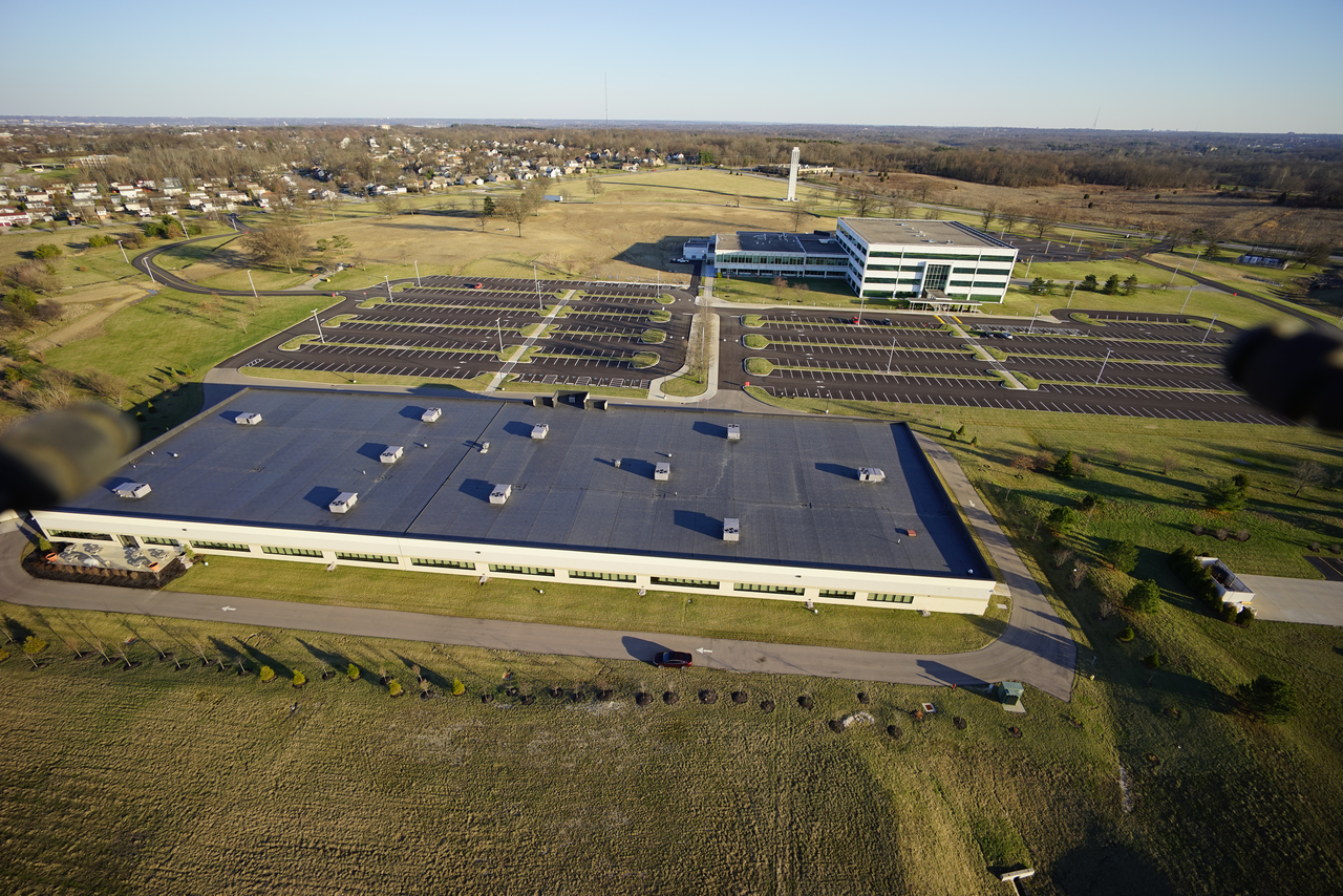 Aerial view of buildings with flat roofs, surrounded by grass and parking lots.