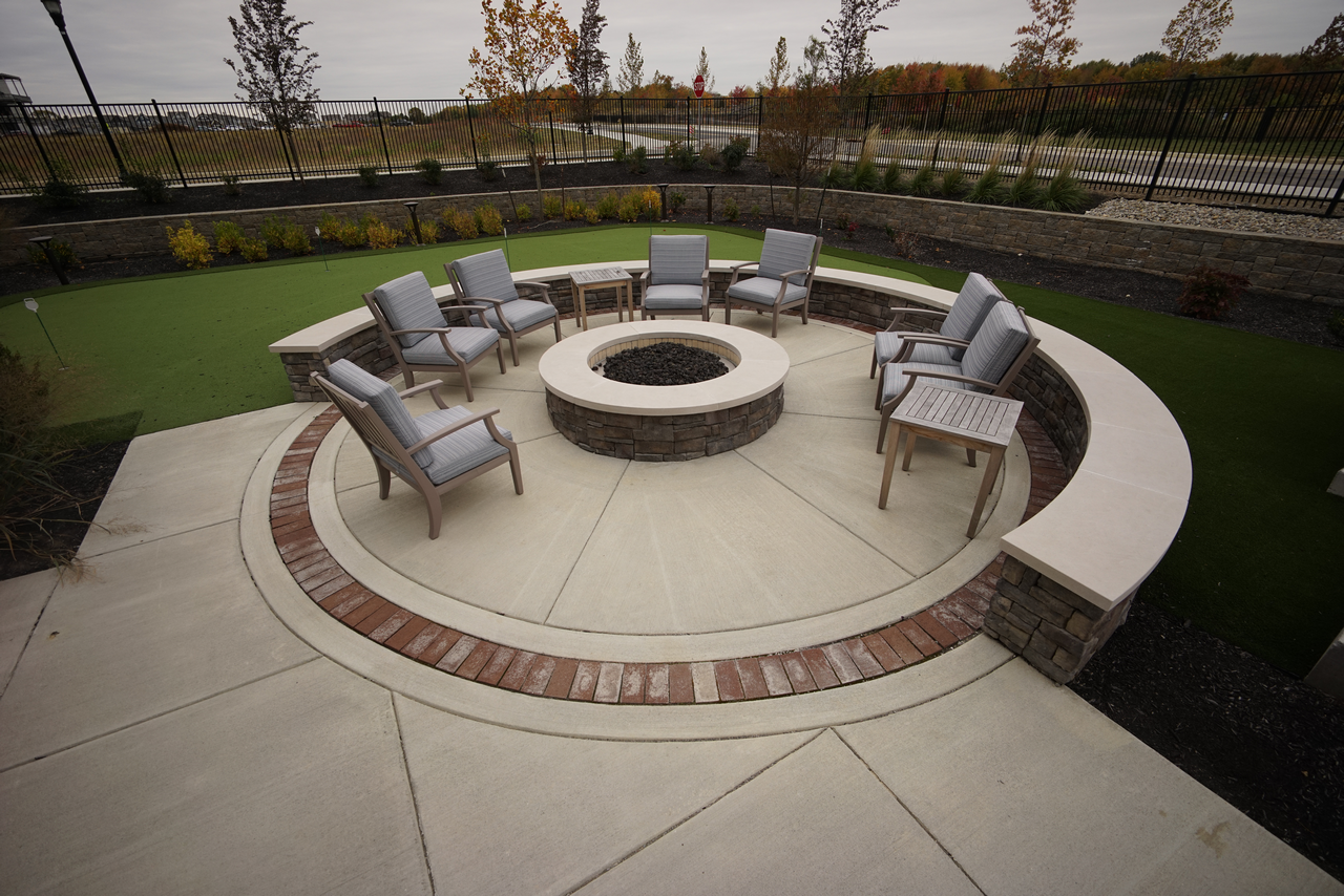 Outdoor fire pit with chairs and curved stone seating under a cloudy sky.