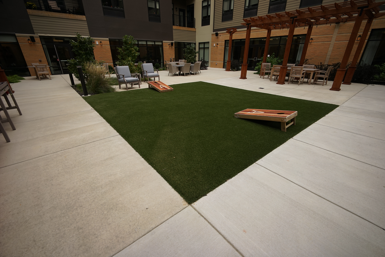 Courtyard with artificial turf, cornhole boards, and seating areas under pergolas.