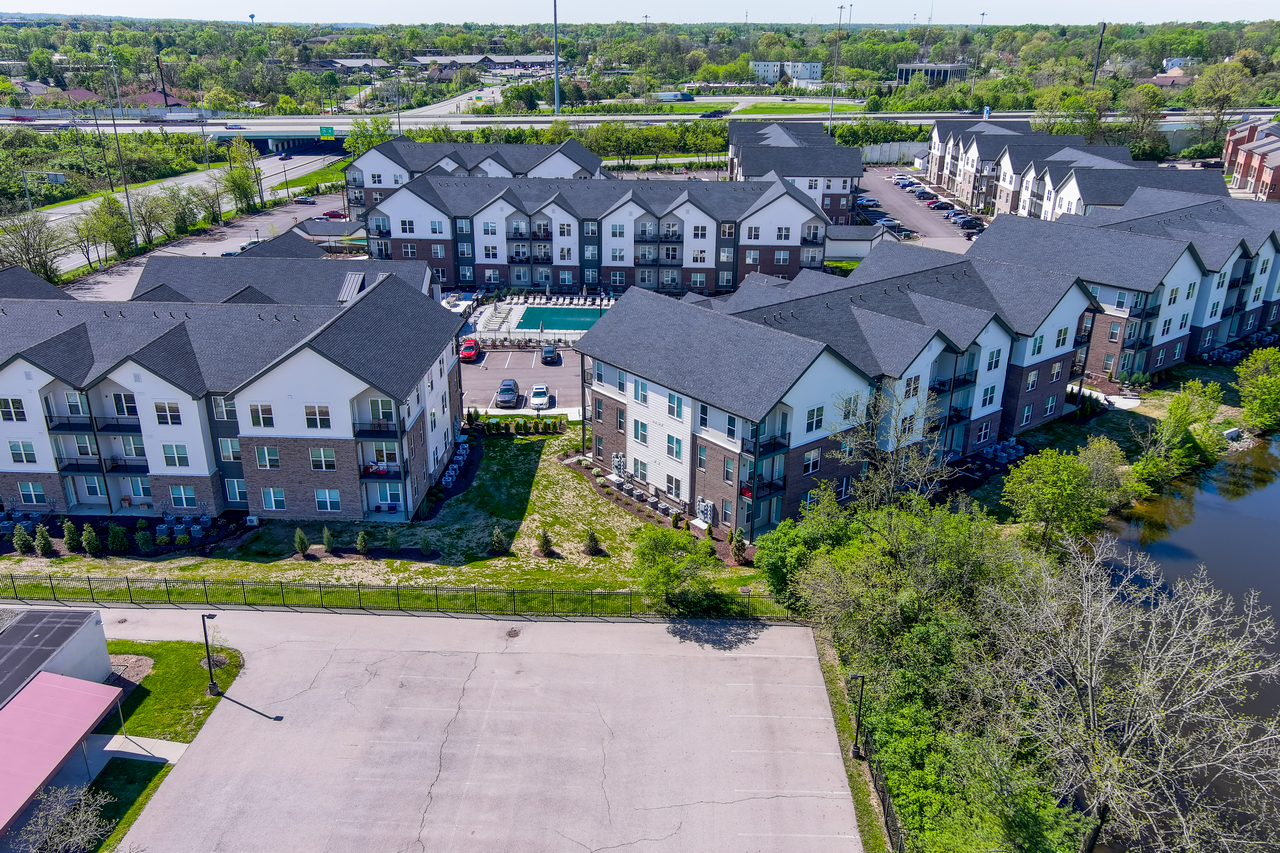 Aerial view of apartment complex with pool, surrounded by greenery.