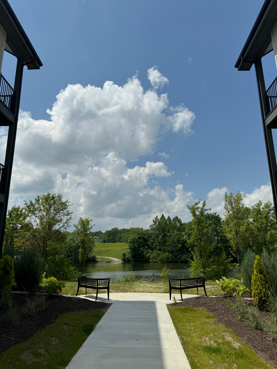 Pathway between buildings leading to a pond under a cloudy blue sky.