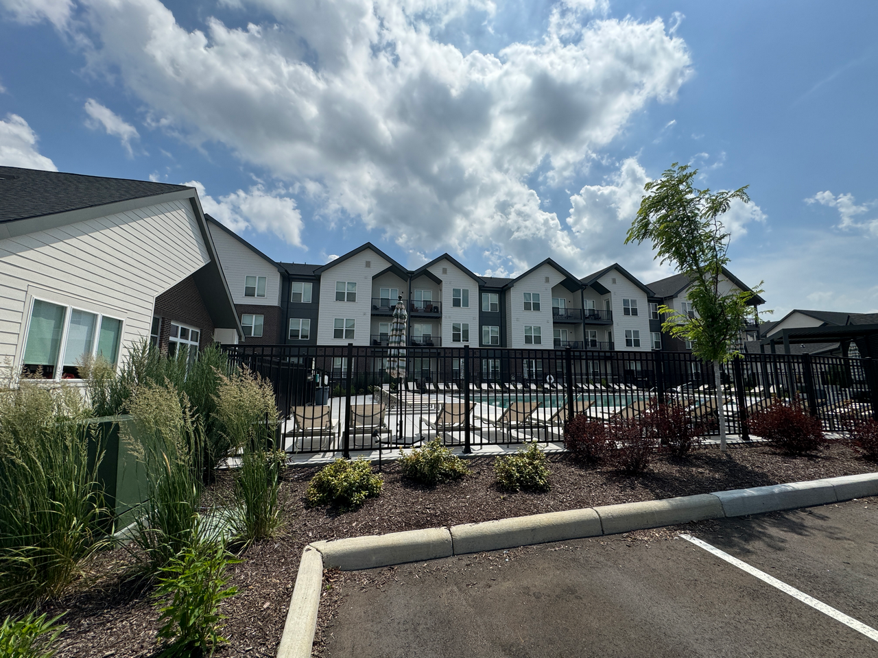 Large building with a pool, surrounded by greenery under a partly cloudy sky.