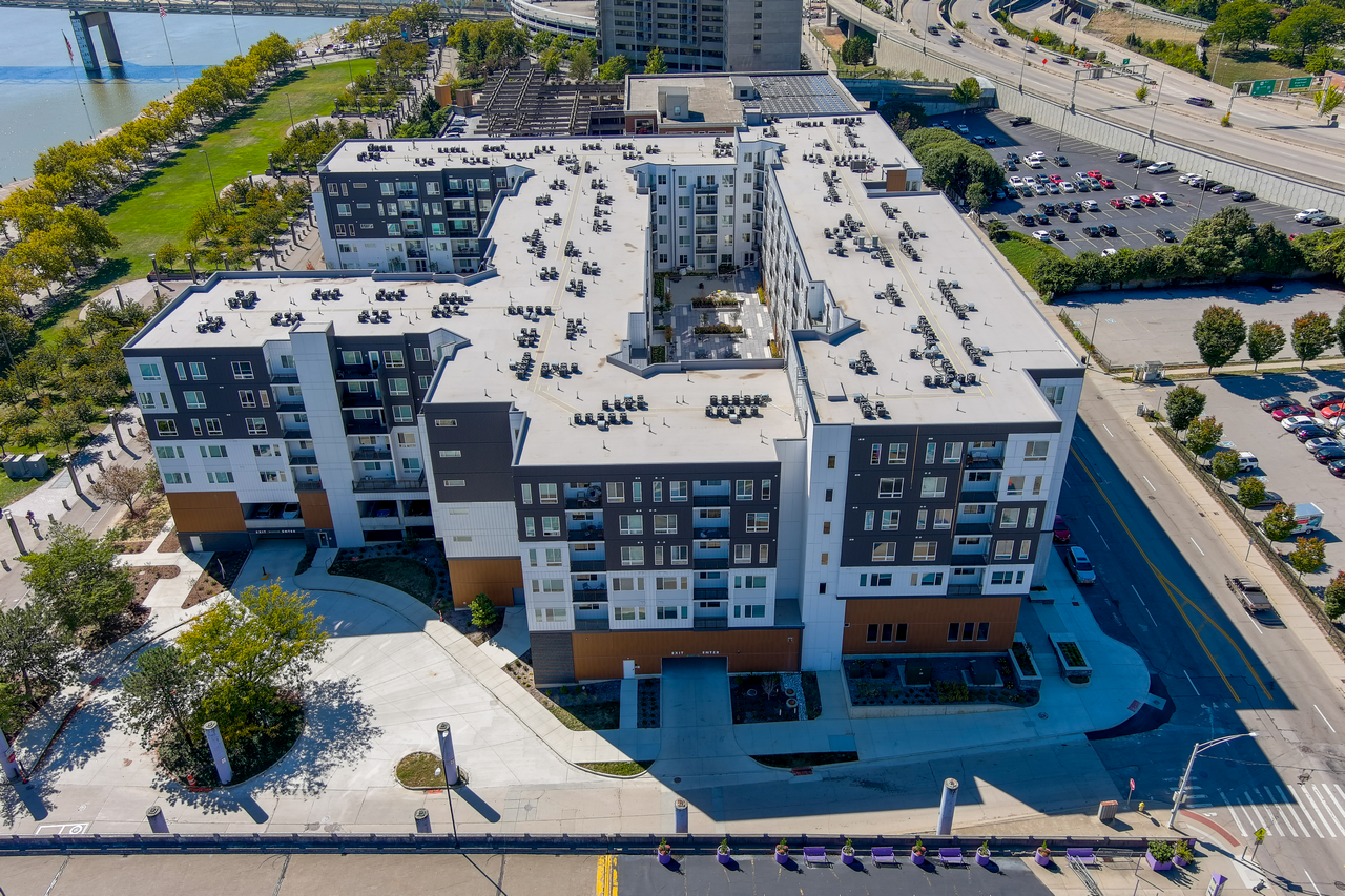 Aerial view of a modern apartment complex near a highway, surrounded by trees.