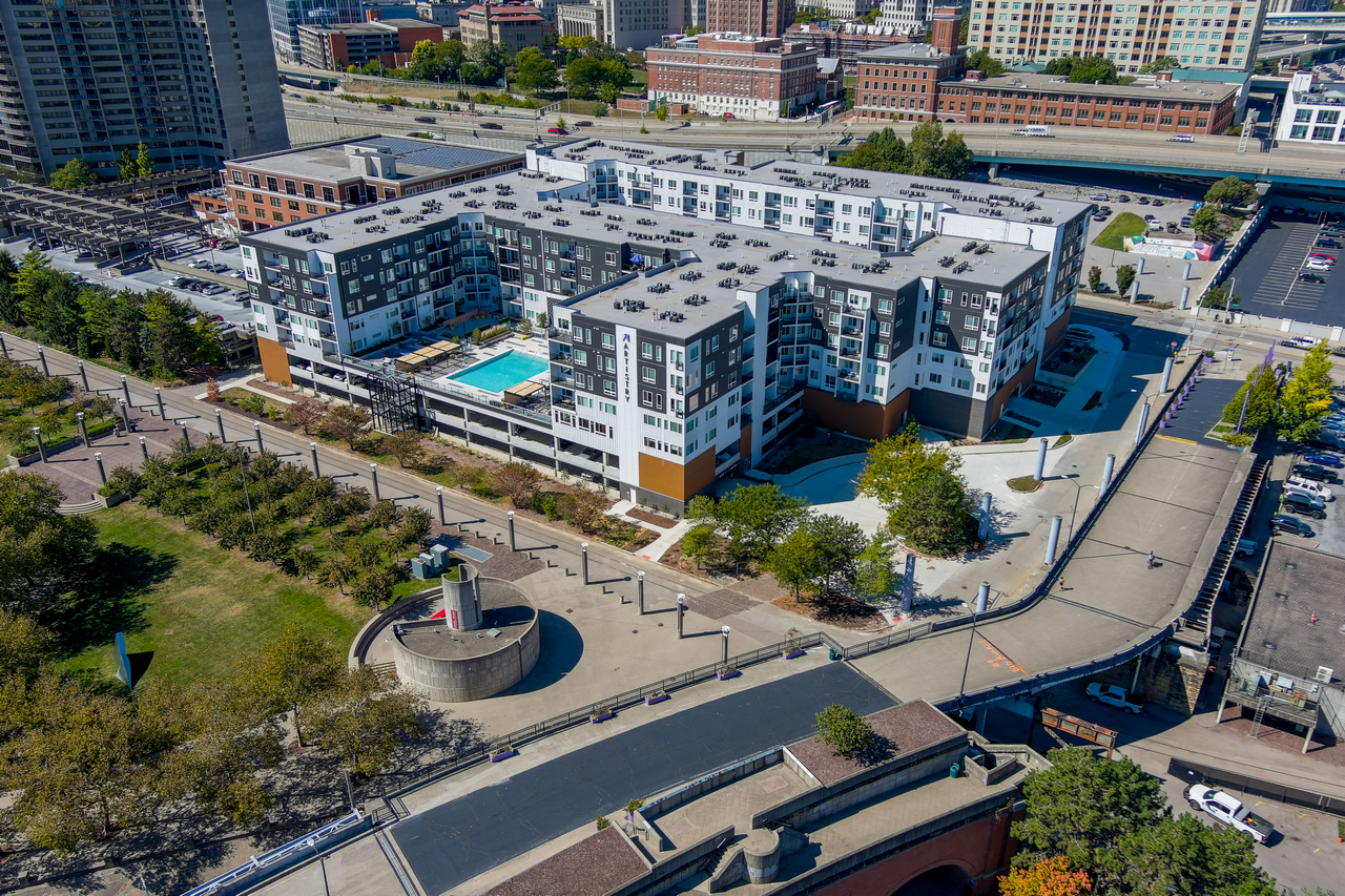 Aerial view of a modern apartment complex with a pool, surrounded by a cityscape.