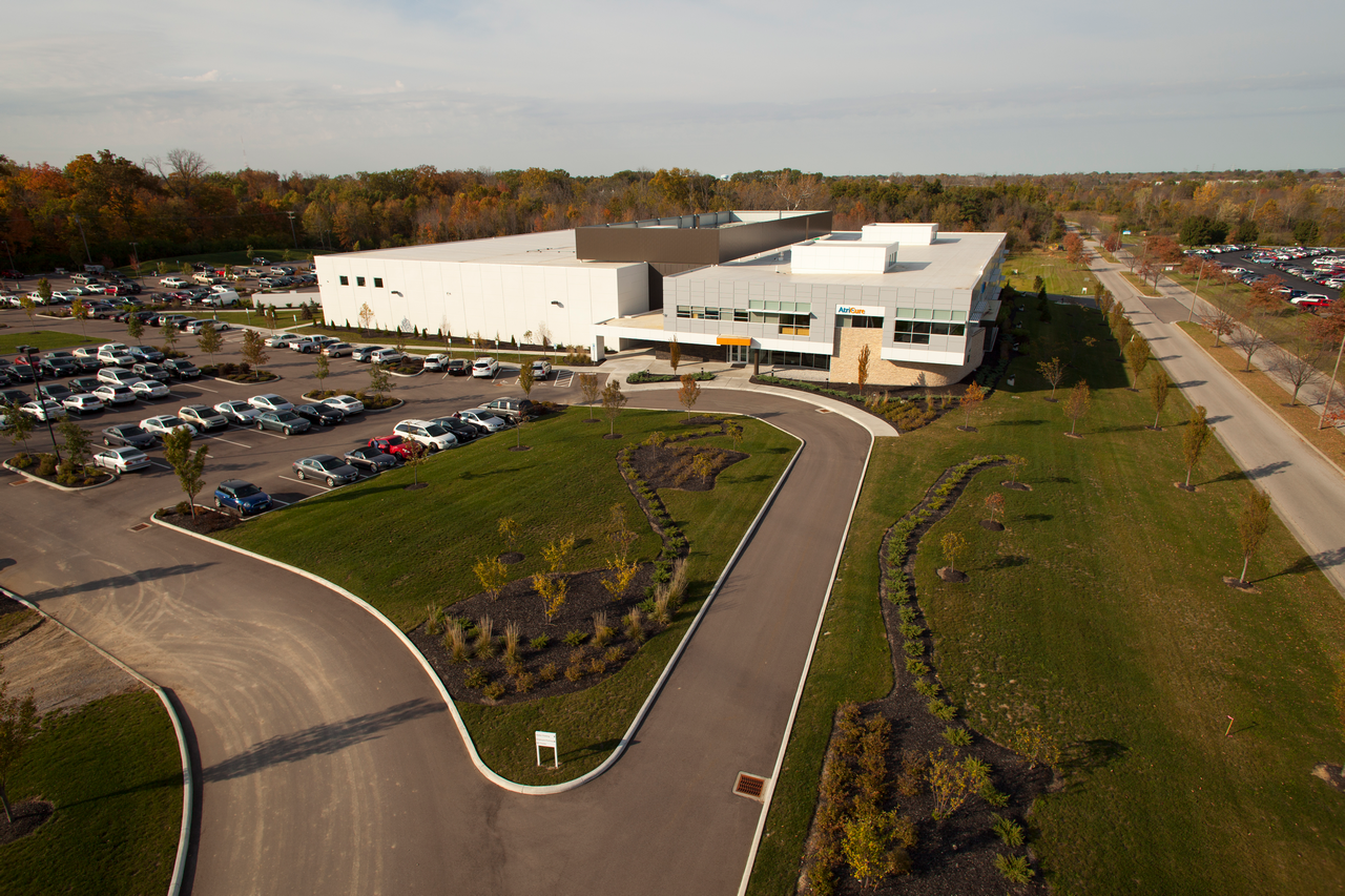 Large white building with adjacent parking lot and landscaped garden.