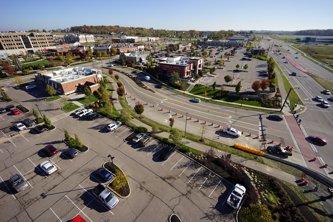 Aerial view of a busy parking lot and road near shops and greenery.