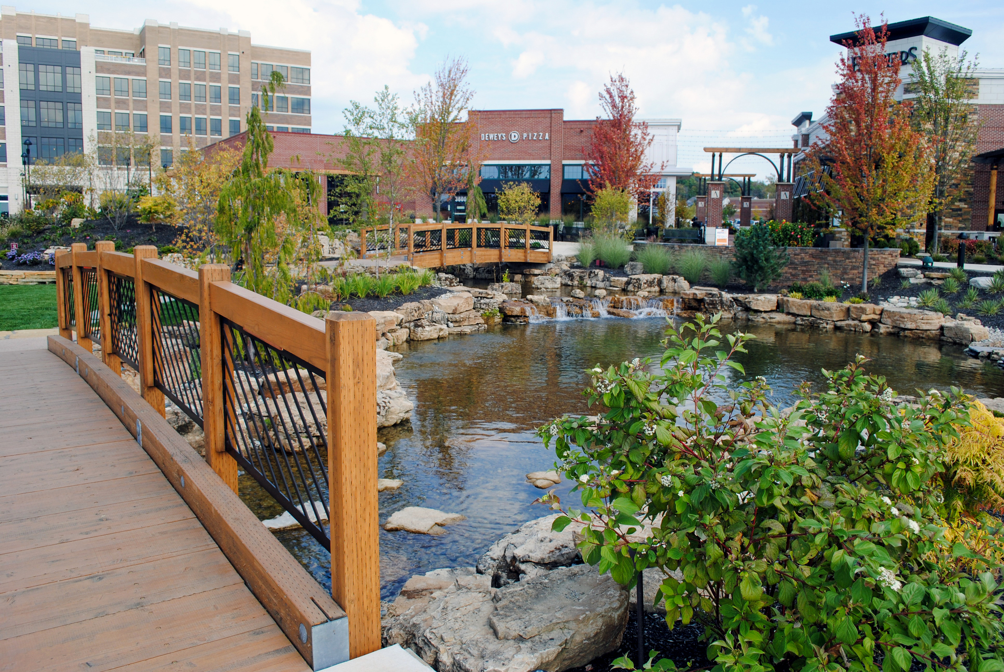 A wooden bridge over a tranquil pond with buildings in the background.