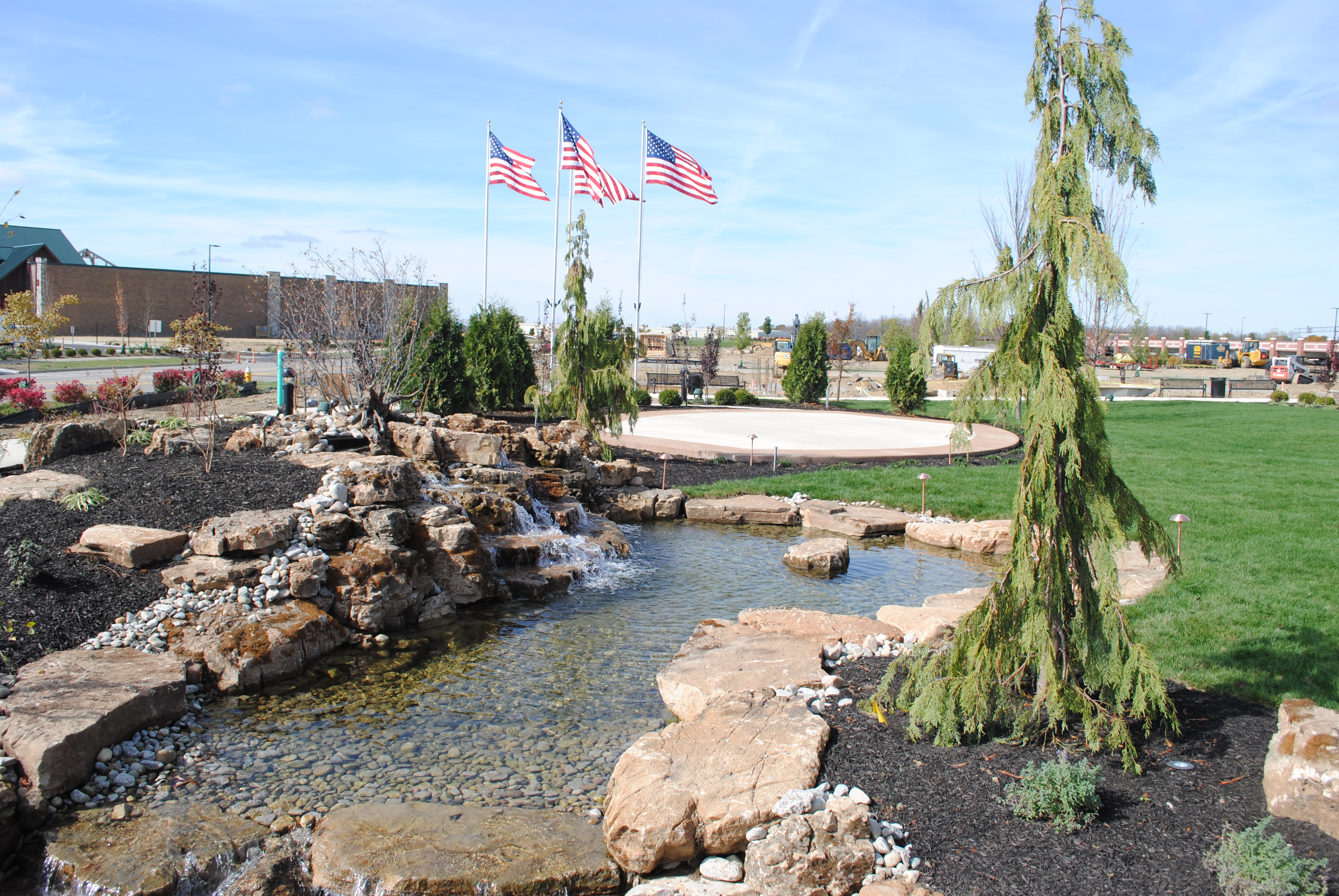 Landscape with pond, waterfall, and three American flags in the background.