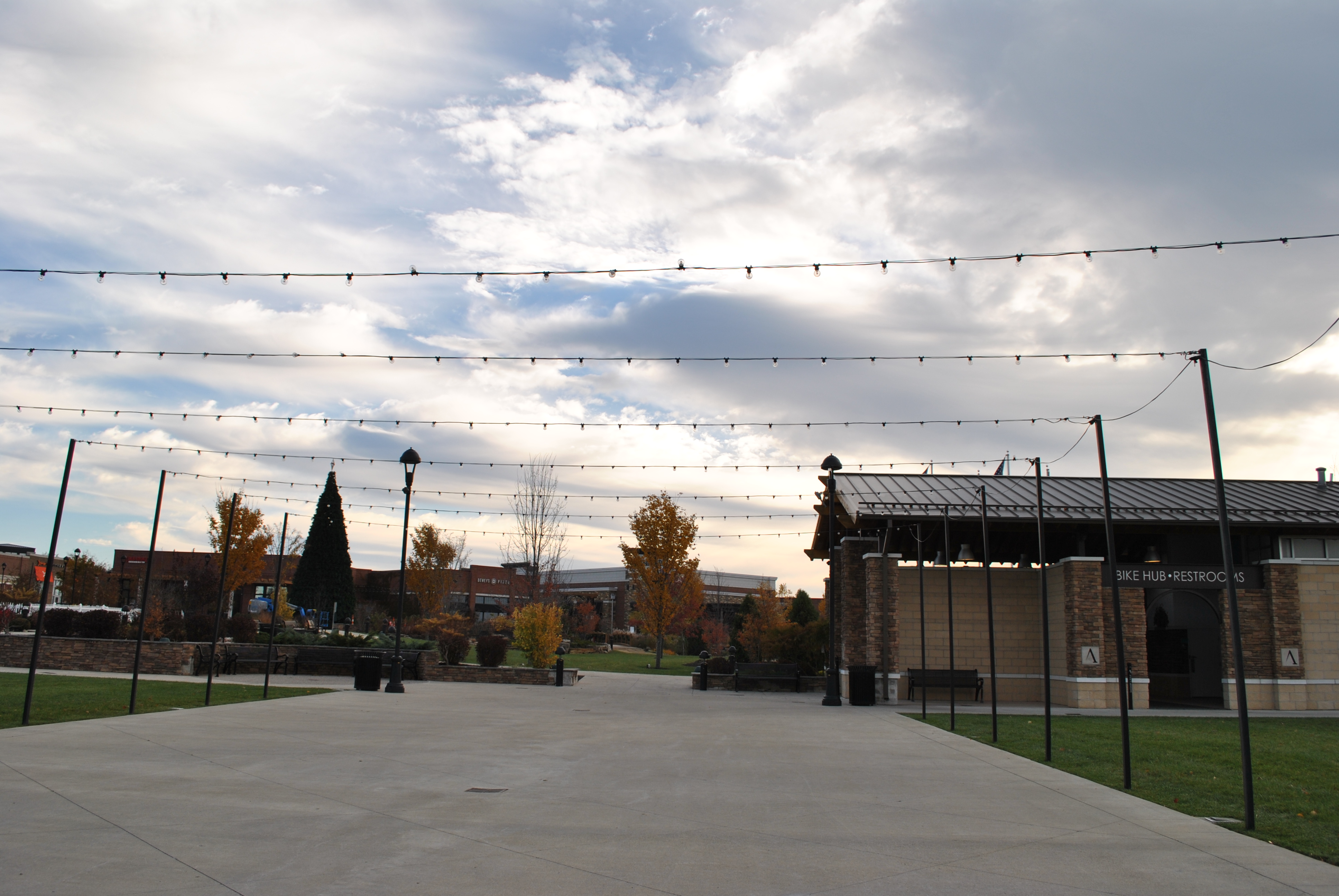 Open plaza with string lights under a cloudy sky.