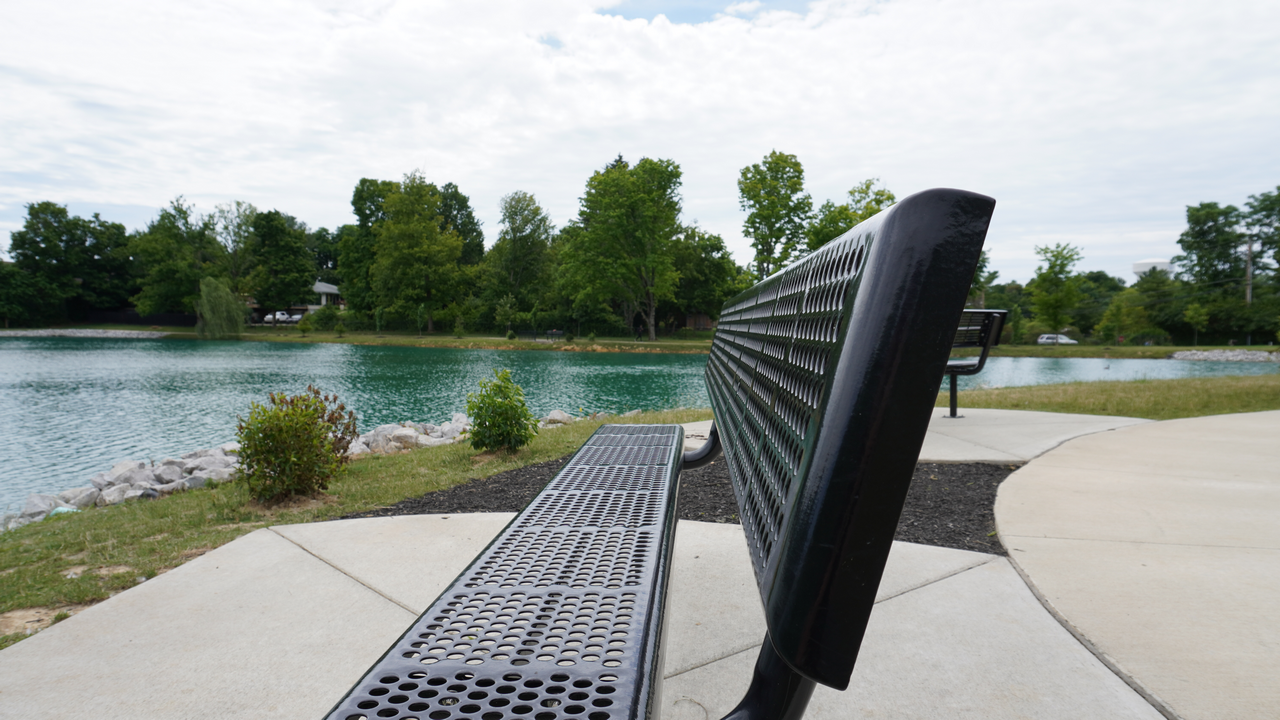 Bench overlooking a calm lake with trees in the distance, under a cloudy sky.