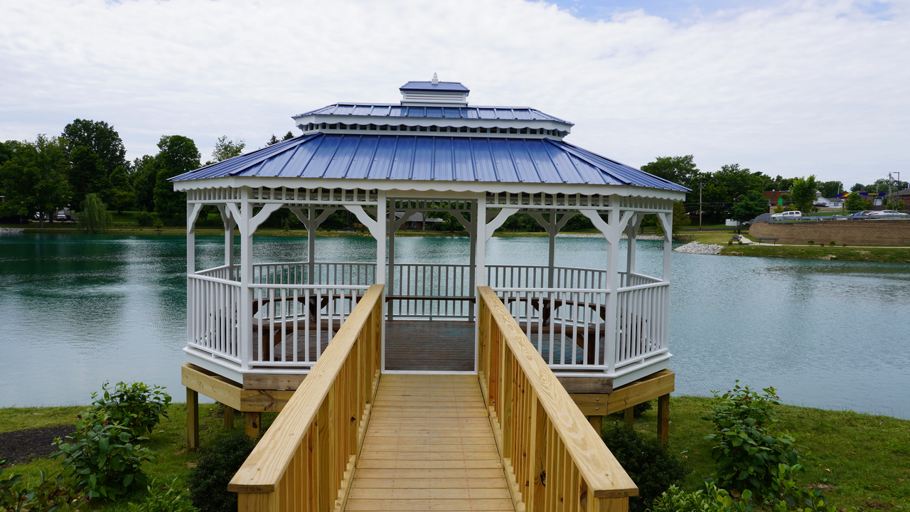 Gazebo with blue roof by a lake, wooden walkway leading to it.