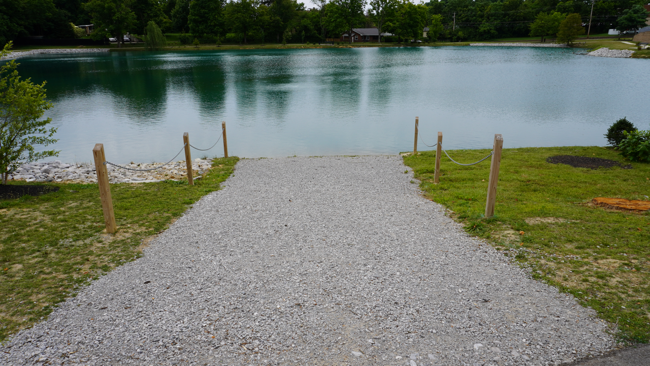 Gravel path leading to a calm lake surrounded by trees.