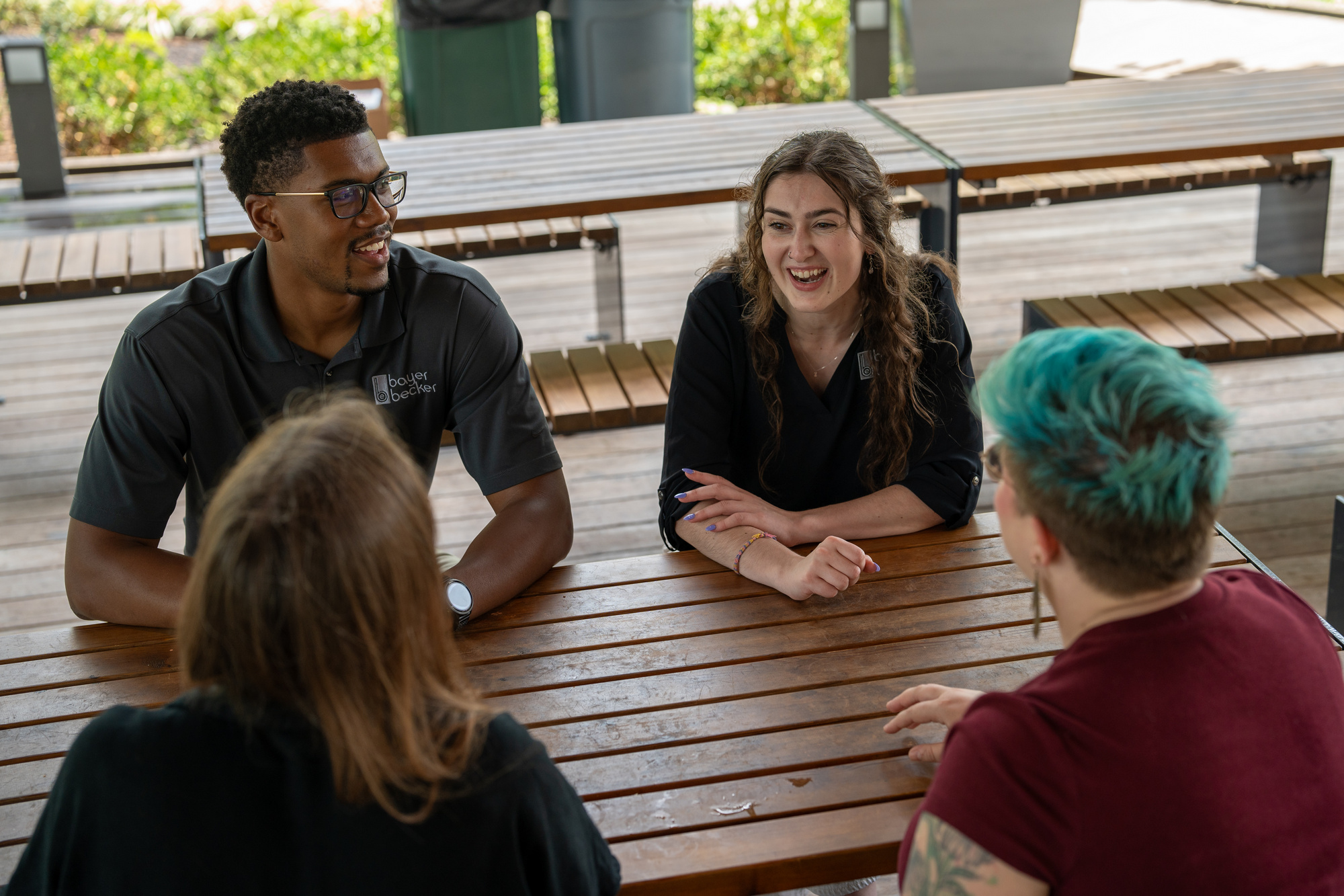Group of four people laughing around a picnic table outside.