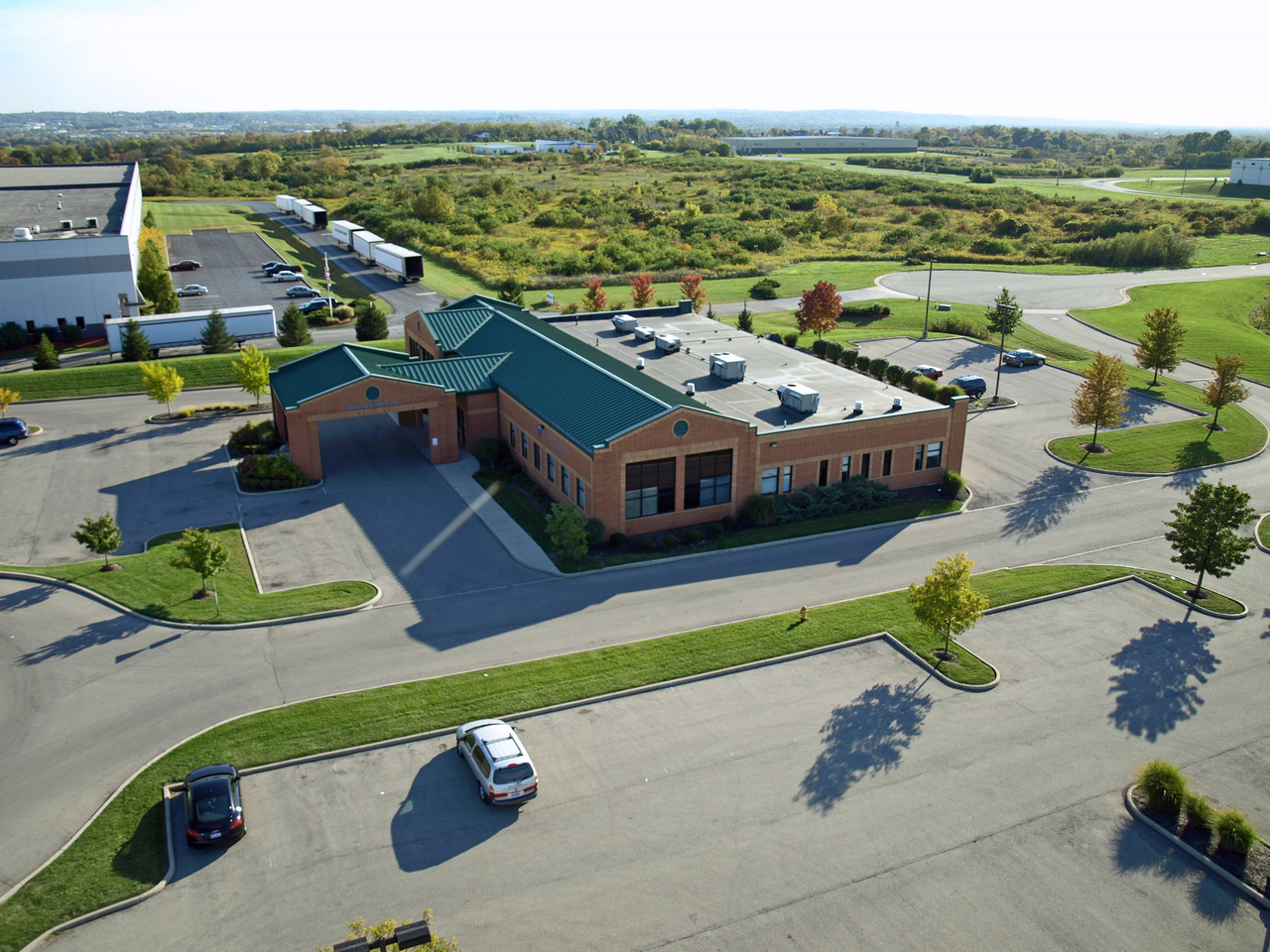 Aerial view of a brick office building with green roof, surrounded by parking and greenery.