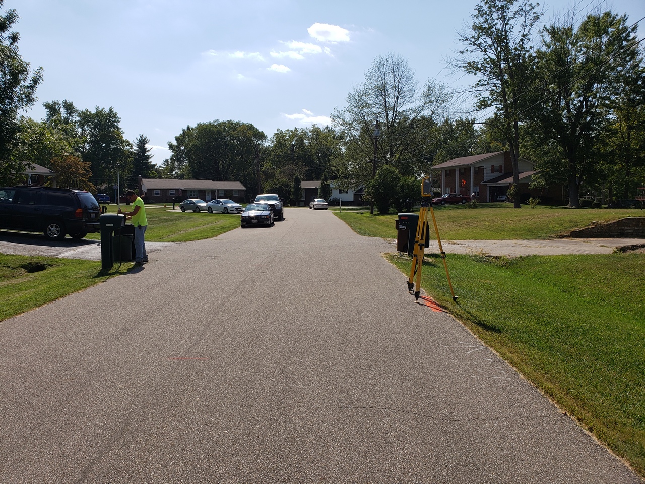 Residential street with a person near a tripod on a sunny day.