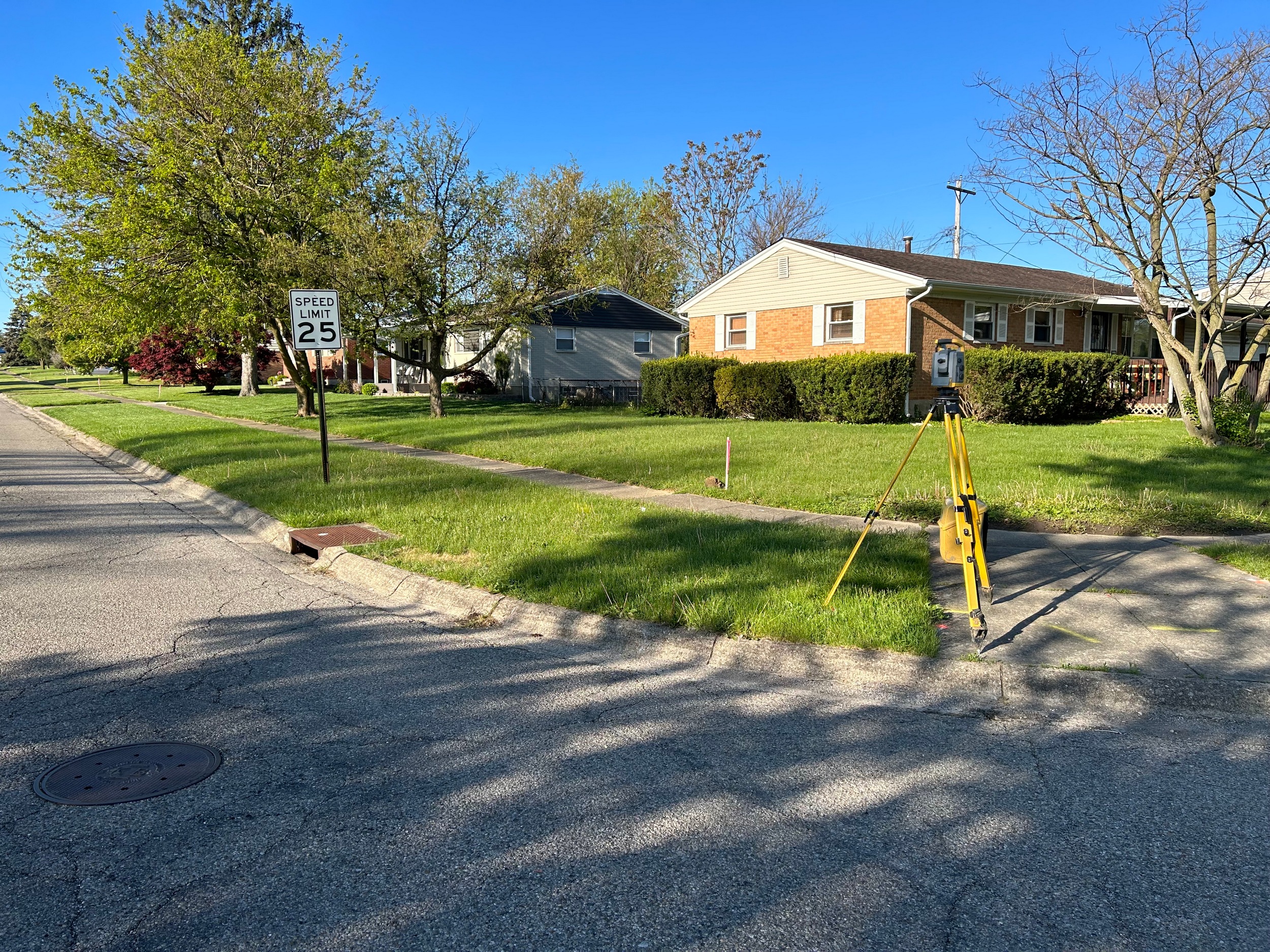 Quiet suburban street with houses, trees, and sunlight casting shadows.