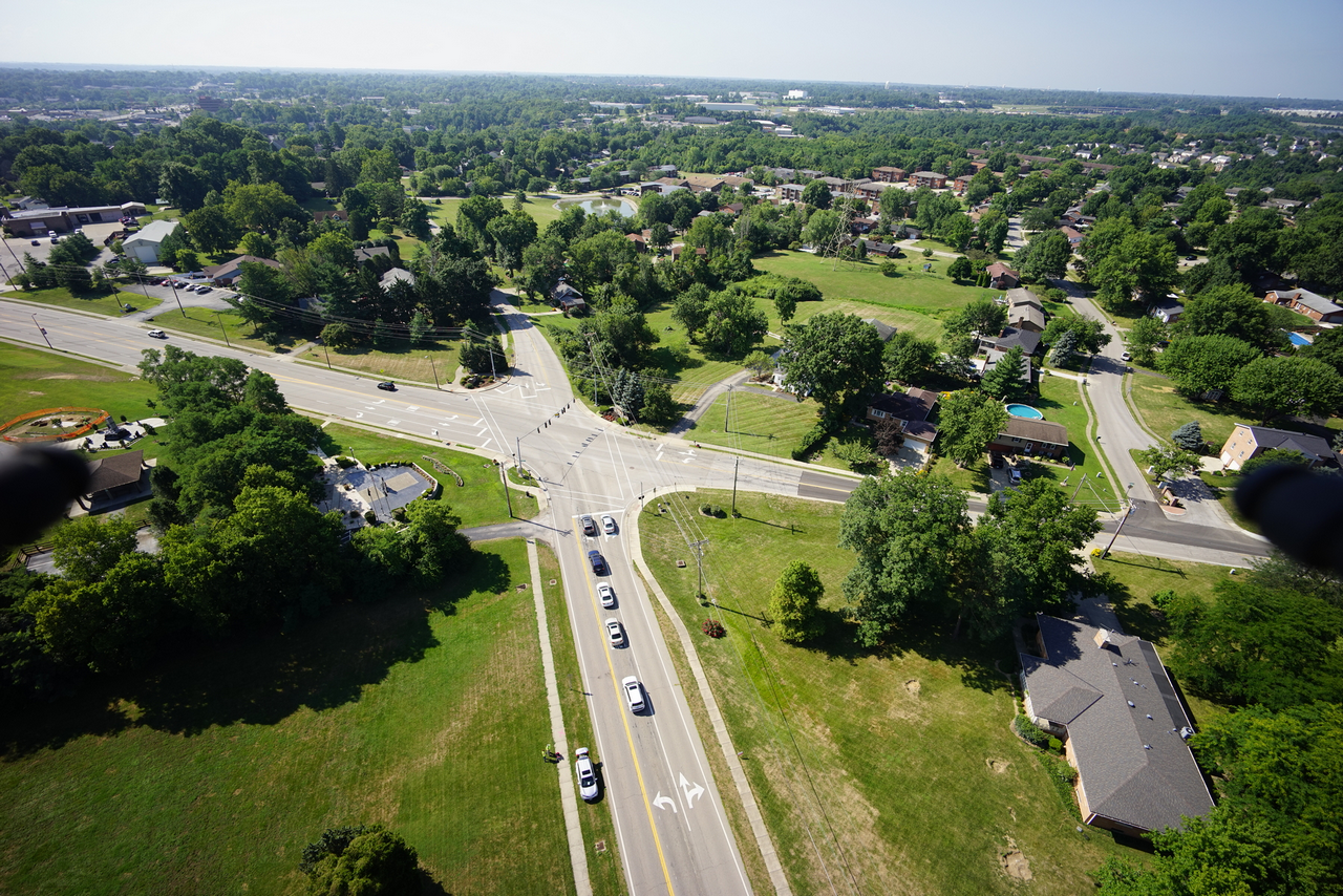 Aerial view of a suburban intersection with green spaces and houses.