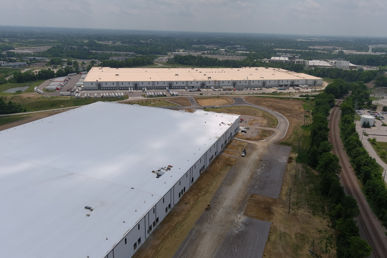 Large warehouses surrounded by roads and greenery on a cloudy day.