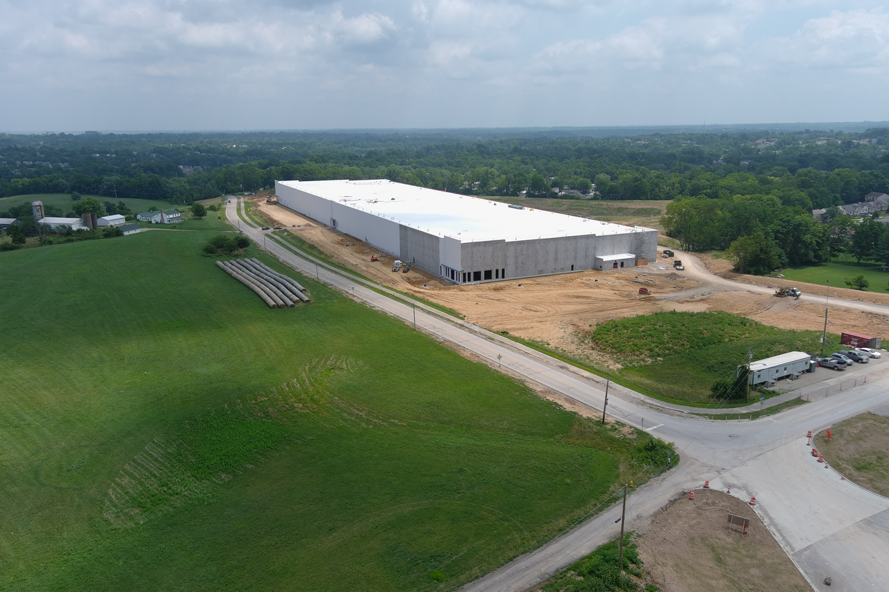 Aerial view of a large warehouse surrounded by greenery and roads.