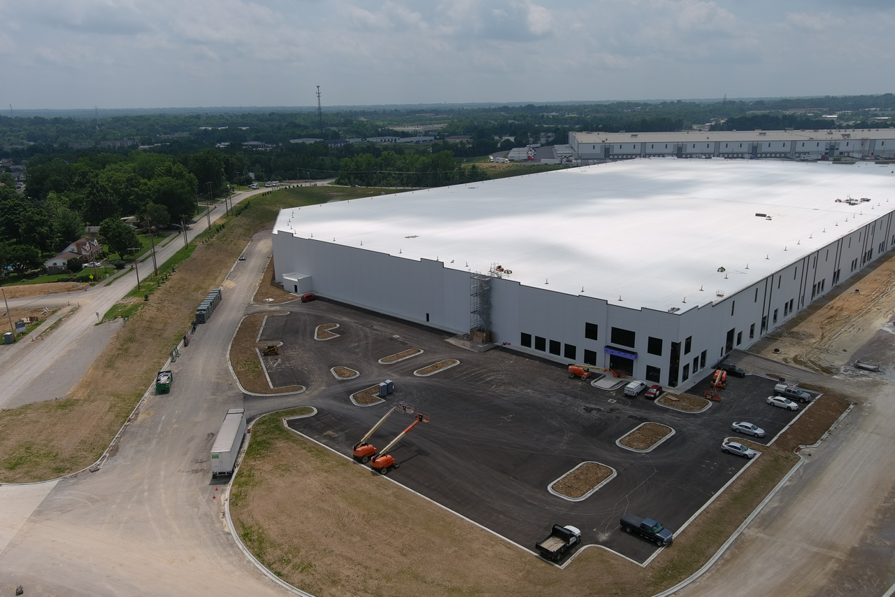 Aerial view of a large warehouse with a white roof and surrounding roads.