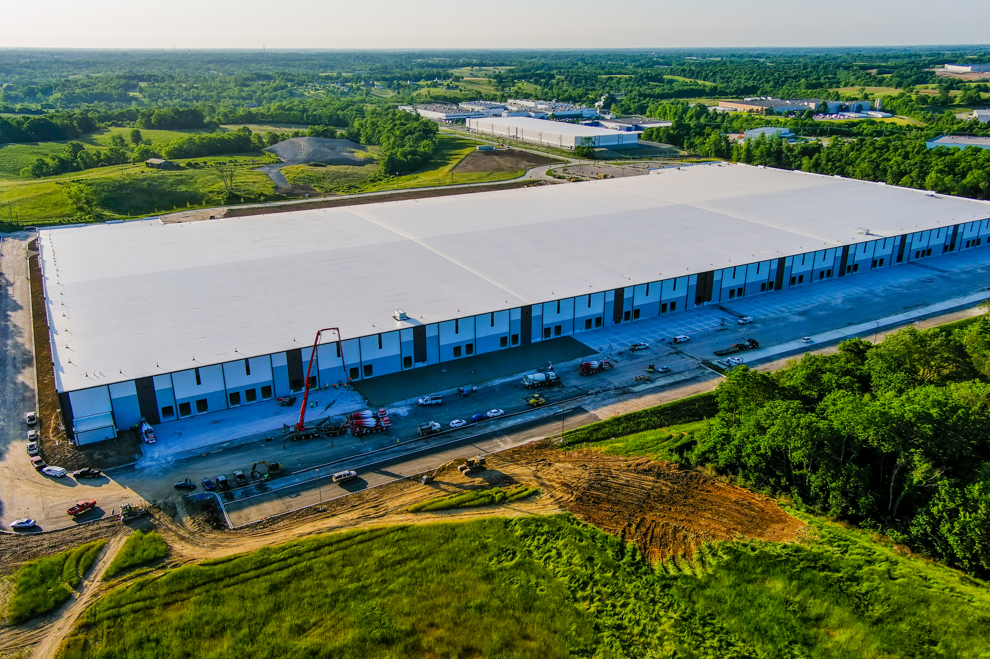 Large warehouse surrounded by green fields under a clear blue sky.