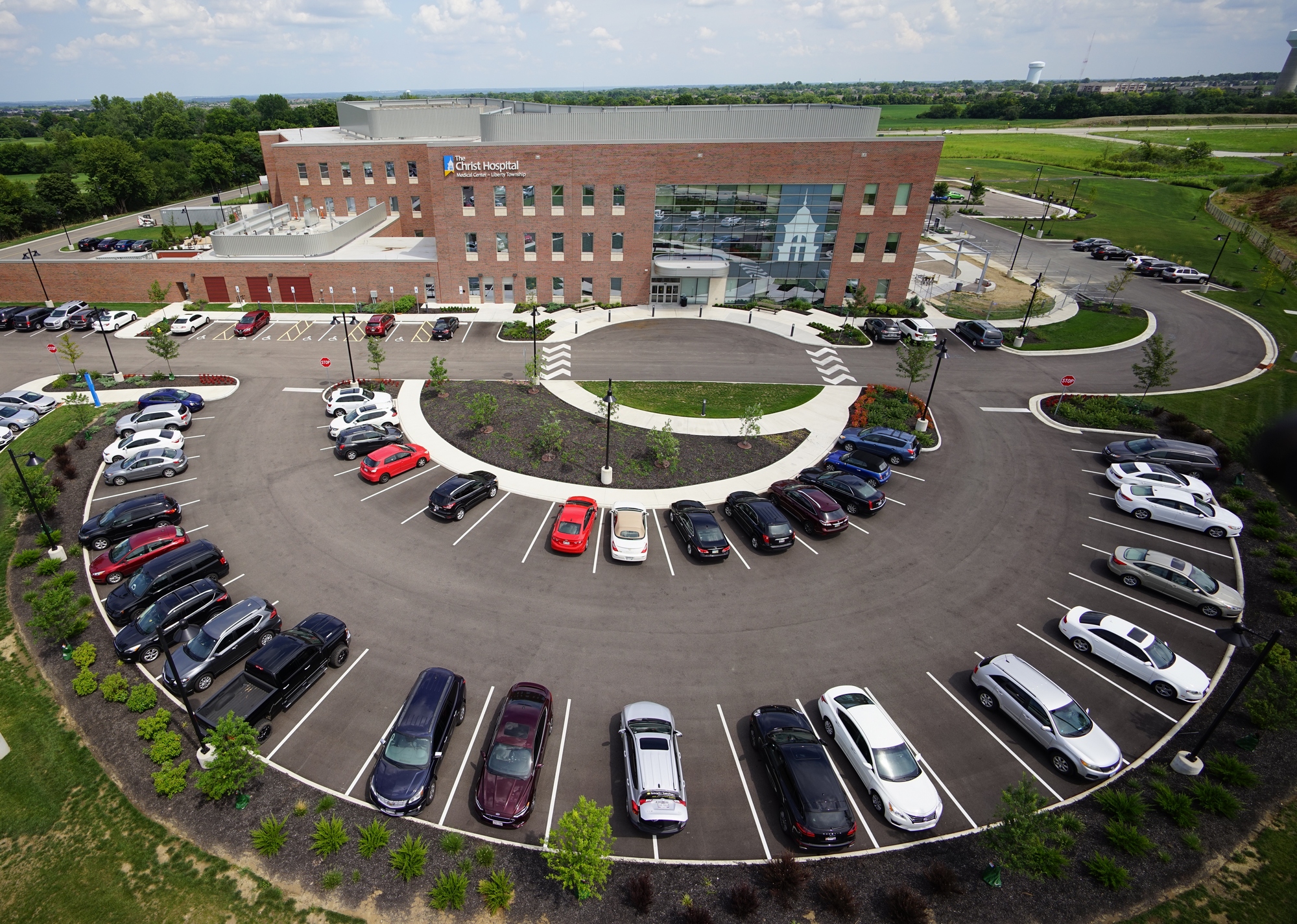 Brick building with circular driveway and parked cars, surrounded by greenery.