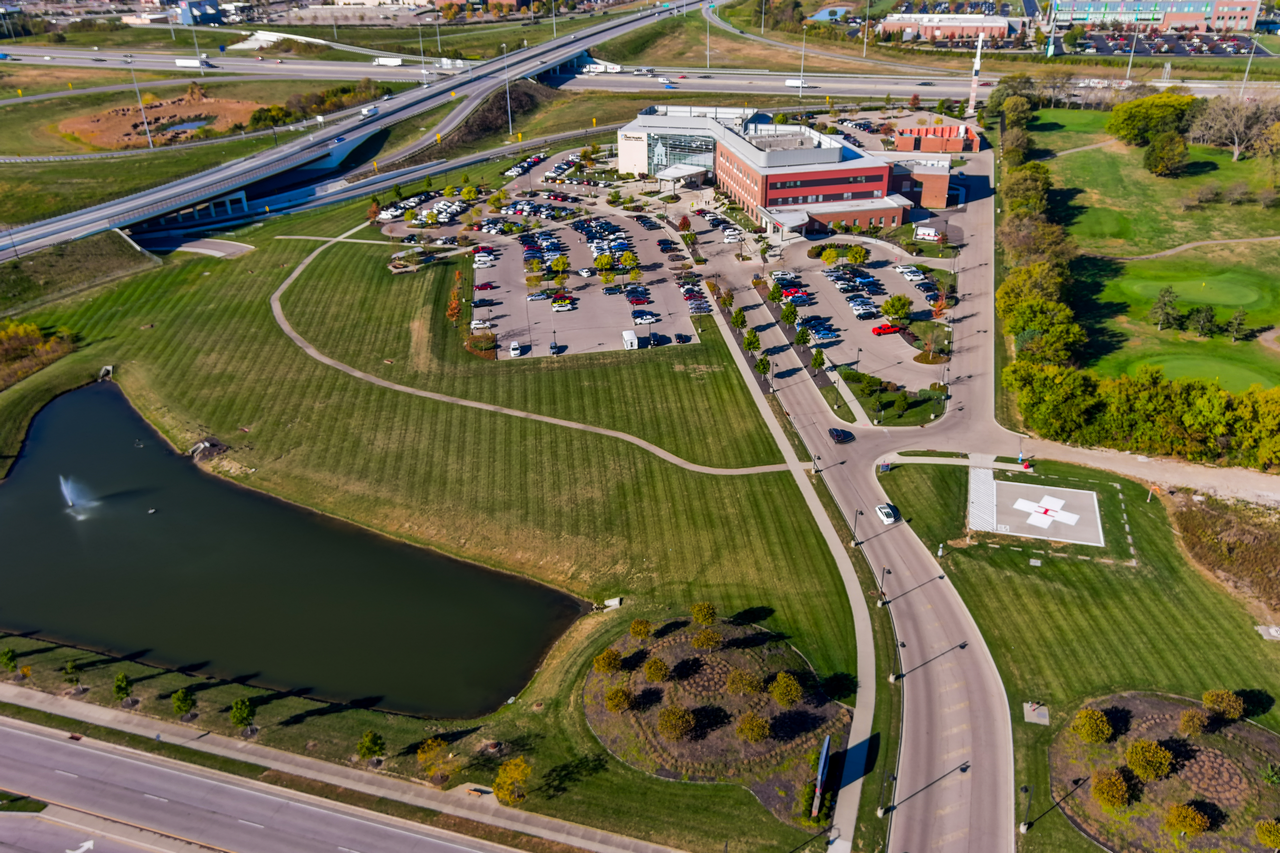 Aerial view of a hospital complex with parking, surrounded by roads and a pond.
