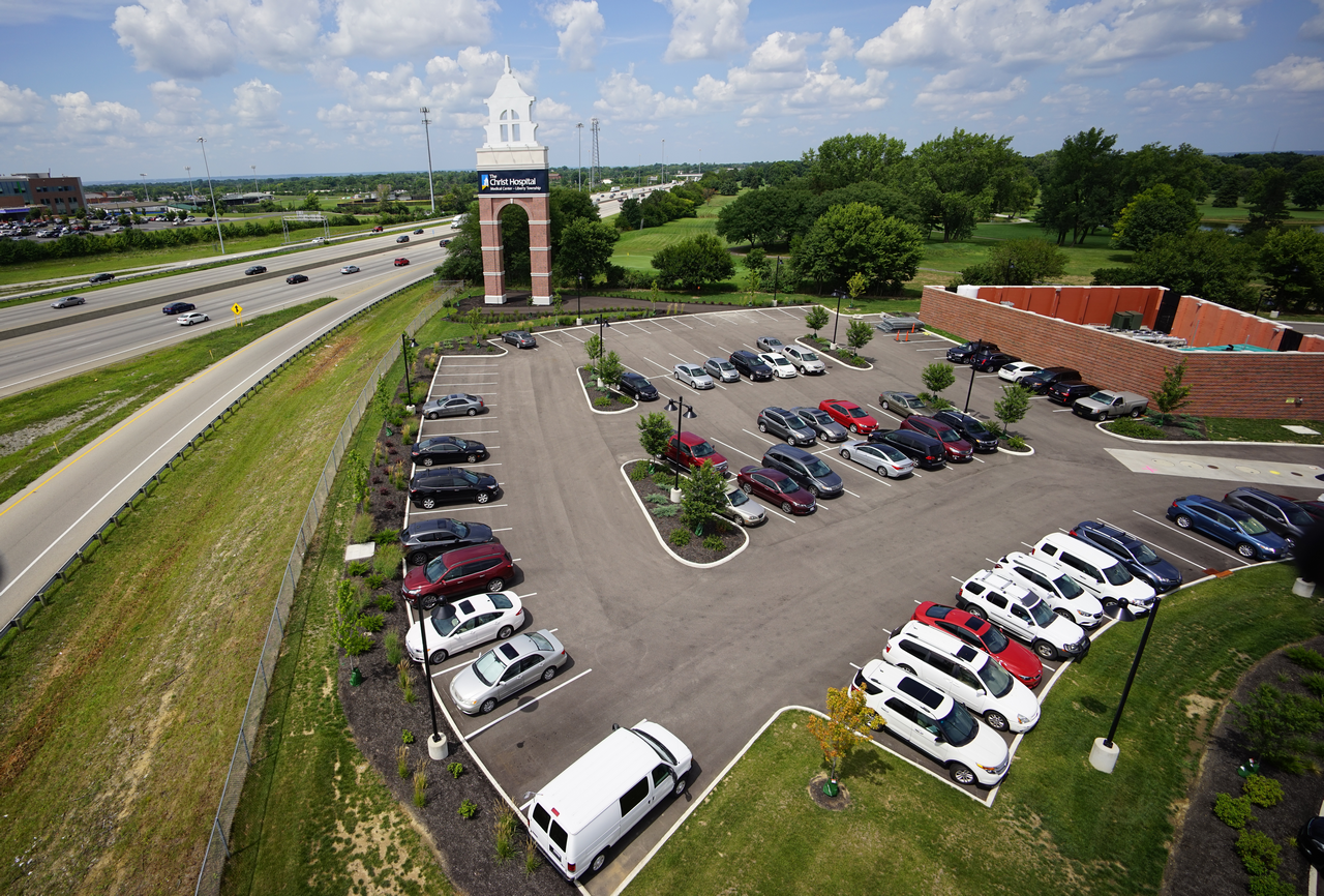 Parking lot with parked cars, adjacent building, and greenery under a blue sky.