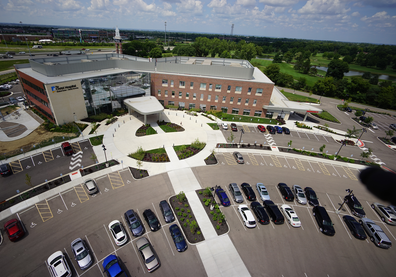 Aerial view of a parking lot and brick building with green lawn and cloudy sky.