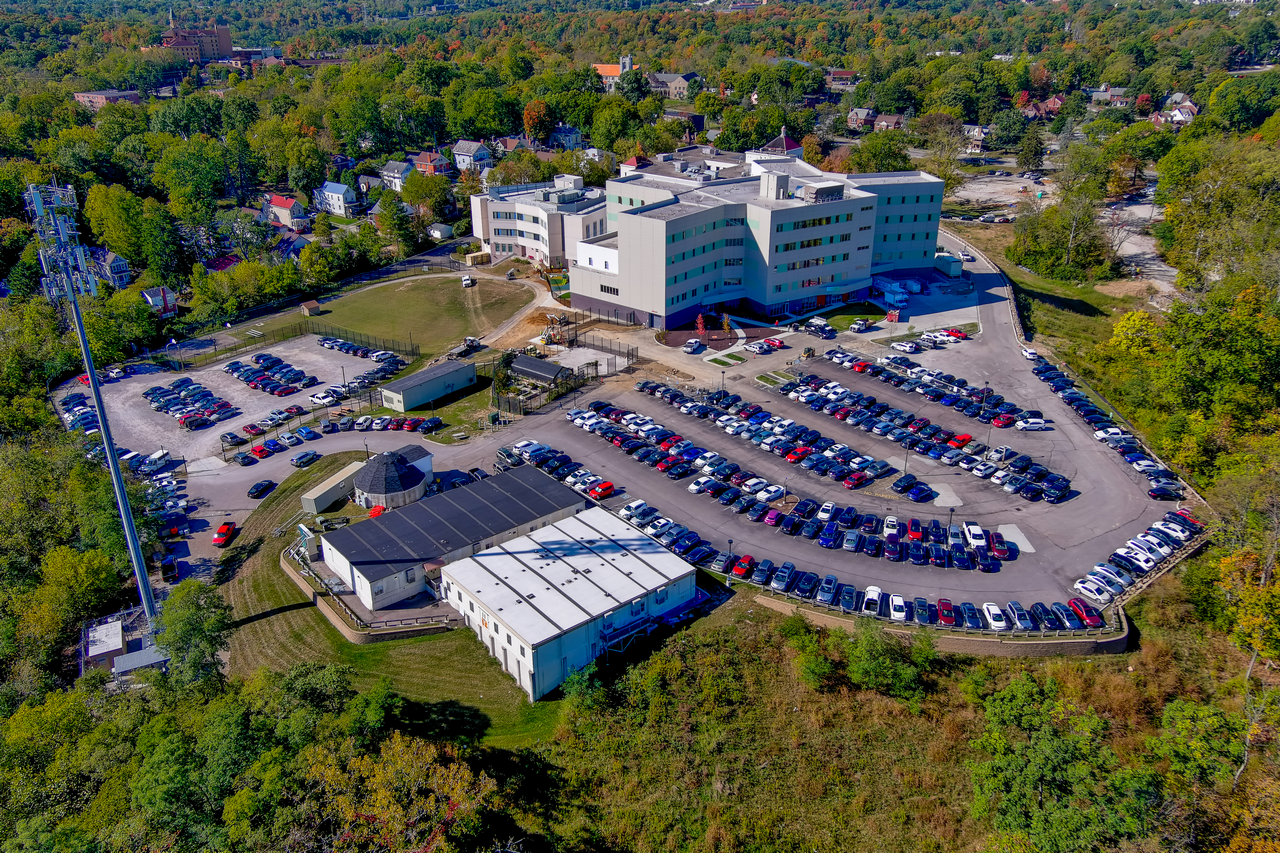 Aerial view of a large building with parking lots, surrounded by trees.