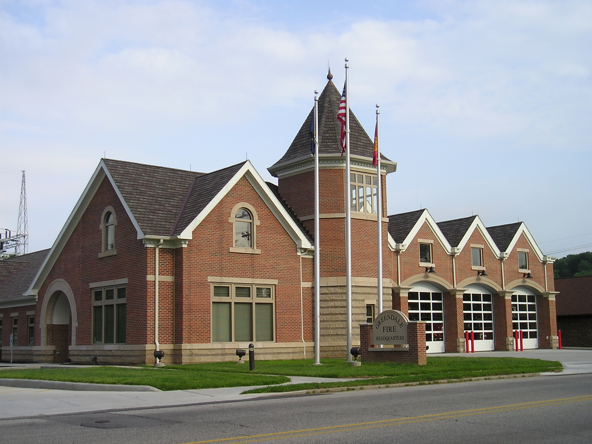 Red brick fire station with tower and flagpoles outside.