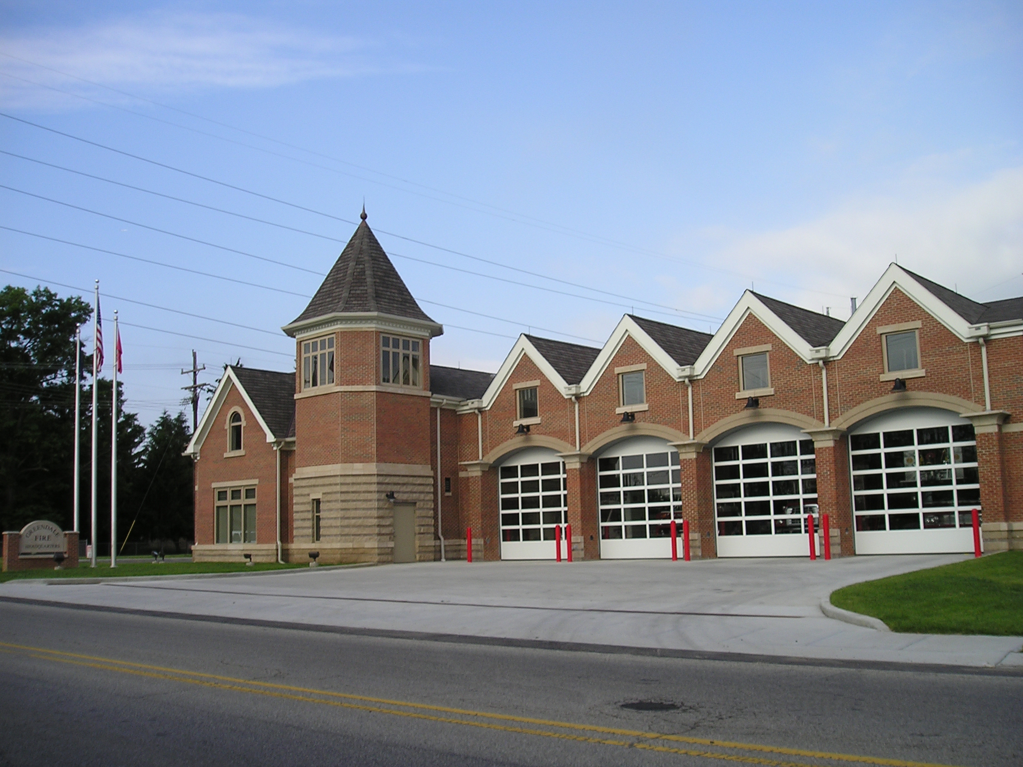 Brick fire station with multiple garage doors and a tower, under a clear blue sky.