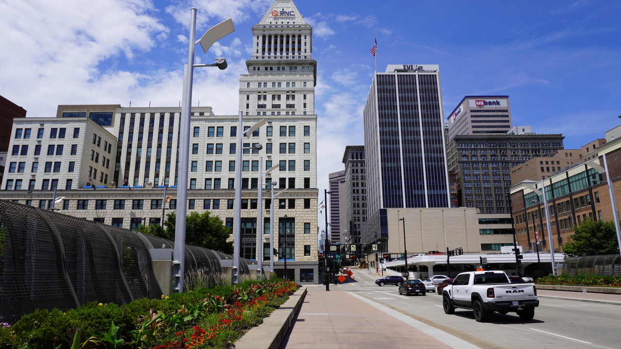 City street with tall buildings, blue sky, and a few vehicles.