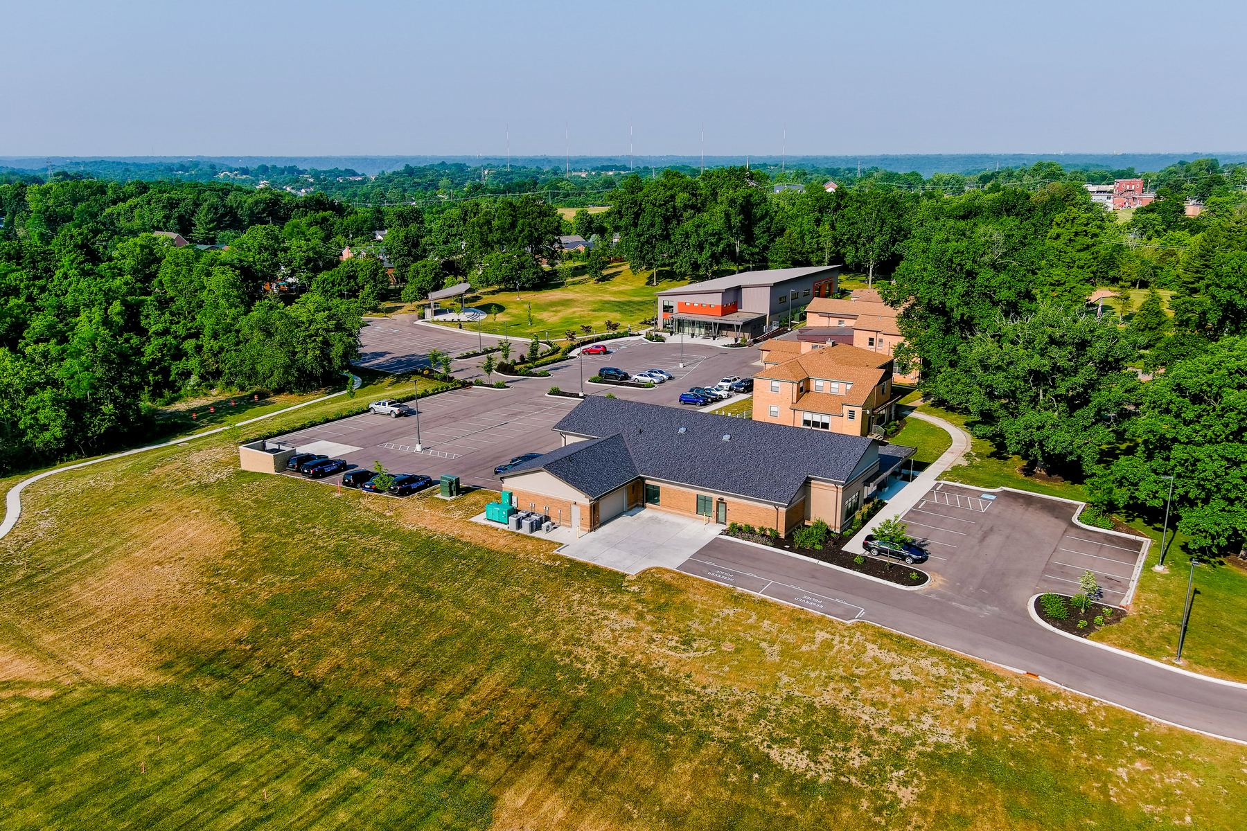 Aerial view of a building complex with parking, surrounded by trees and fields.